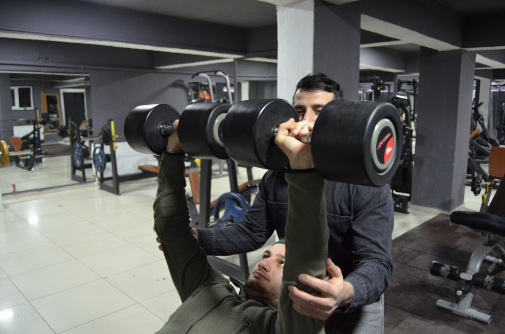 Spor salonunda bench press antrenmanı, eğitmen gözetiminde