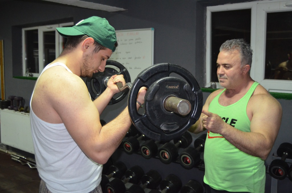 İki sporcu halter ile curl antrenmanı yapıyor